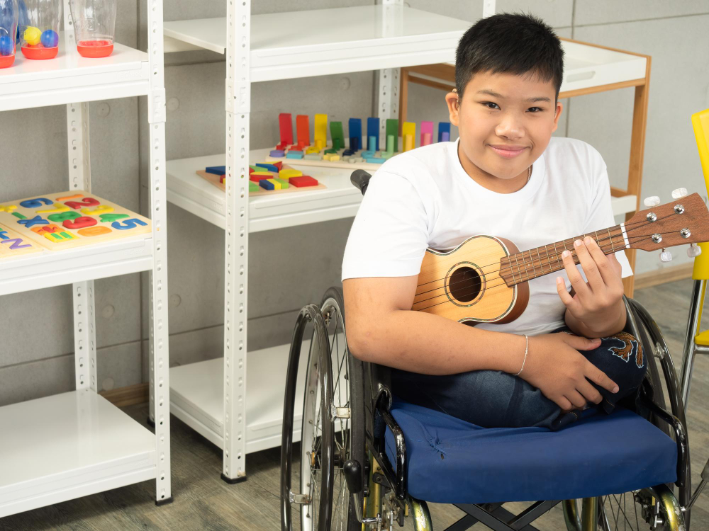 anak lelaki difabel disabilitas tersenyum sambil melihat kamera dan memegang gitar